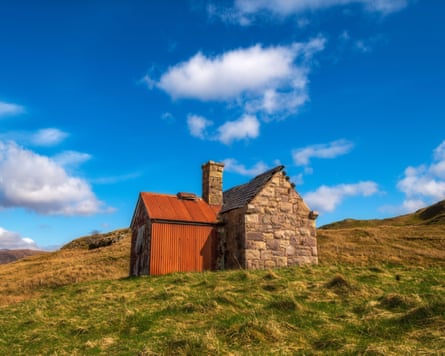 One stone and one tin bothie amid a grassy landscape, with a bright blue sky