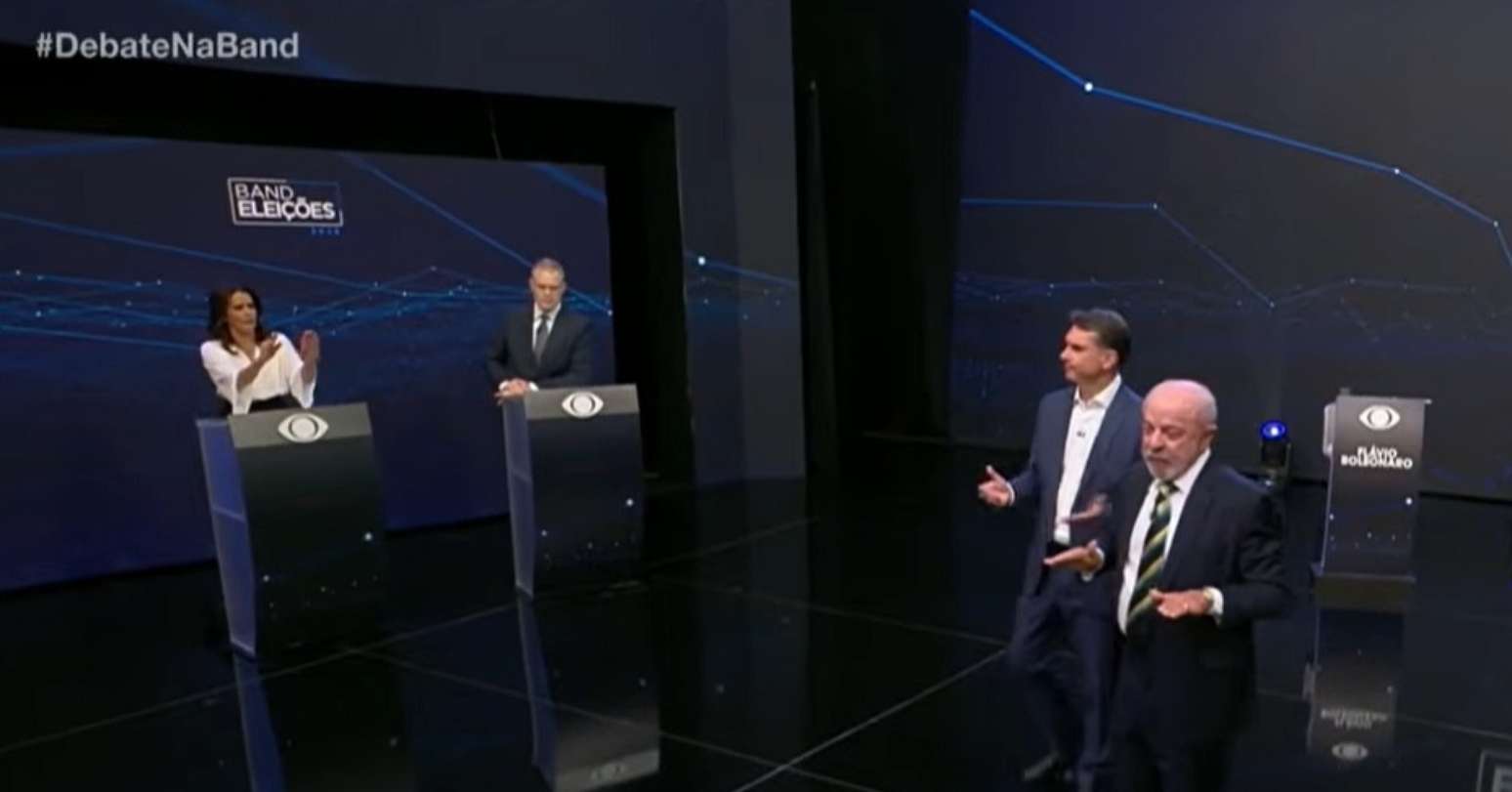 Um dos momentos tensos do debate na Band: os mediadores Adriana Ara&uacute;jo e Eduardo Oinegue precisaram erguer a voz para Fl&aacute;vio Bolsonaro (PL), Lula (PT) e a plateia no est&uacute;dio